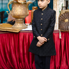 Young boy in formal attire standing next to a decorative urn with a red draped tablecloth in the background.